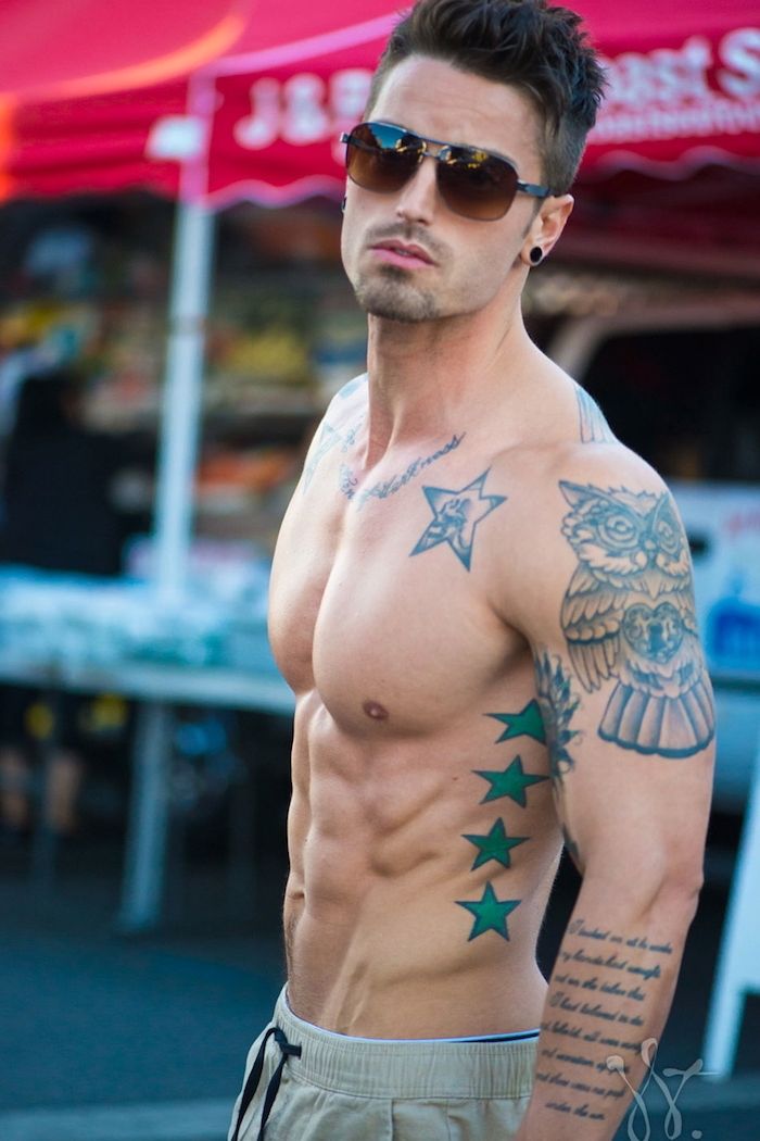 mladý muž s okuliarmi - muž s hviezdou tetovanie so zelenými hviezdami a veľké tetovanie so sovou