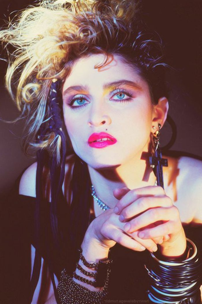 Roupas dos anos 80 - Madonna em uma roupa punk com blusa preta sem alças, muitas pulseiras e acessórios enormes