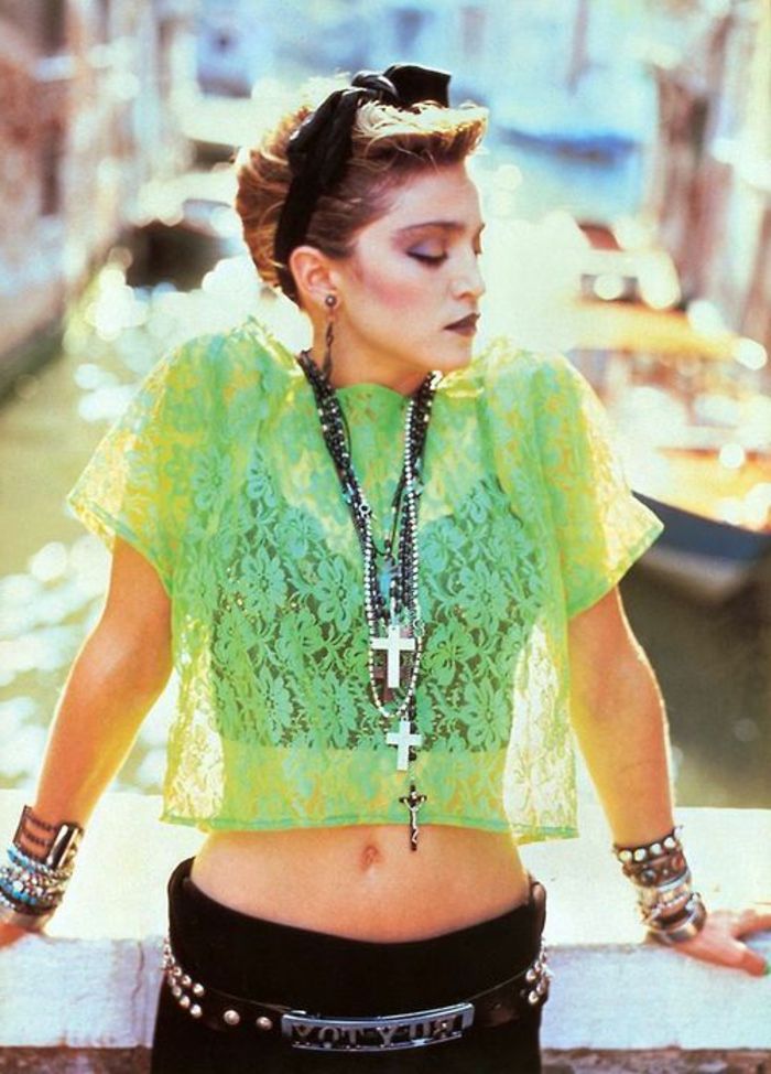 Madonna nos anos 80 com uma blusa de tule verde, faixa de cabelo preta, calça preta e muitas pulseiras