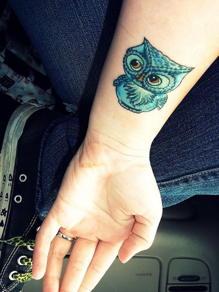 Rankas su pelėda tatuiruote ant riešo - mėlyna maža pelėda su geltonomis akimis