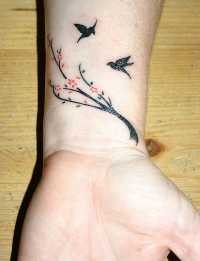 en liten tatuering på en kvinnas handled, svart träd, svarta fåglar