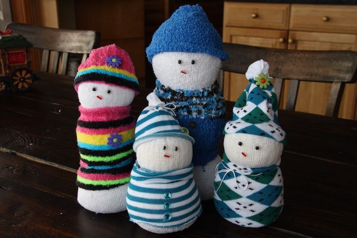 štiri bele snežaki iz belih nogavic in s črnimi očmi in malo vijolično rožo ter s klobuki - snežaka