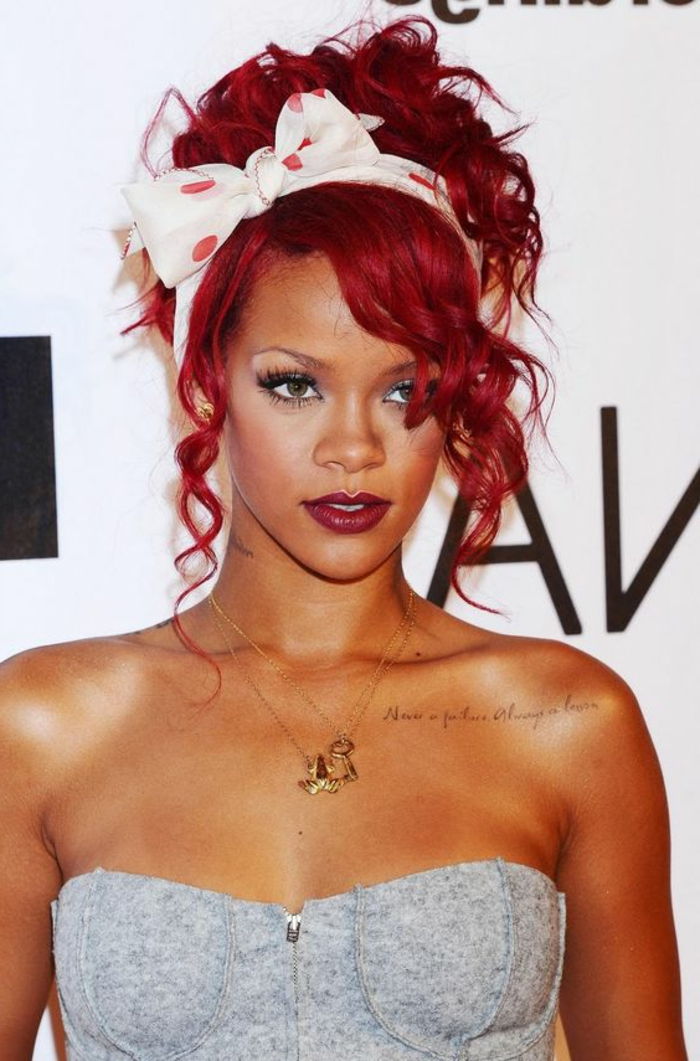 Rihanna med ljust rött hår, vitt hårband med röda prickar, guldkedjor, grå topp