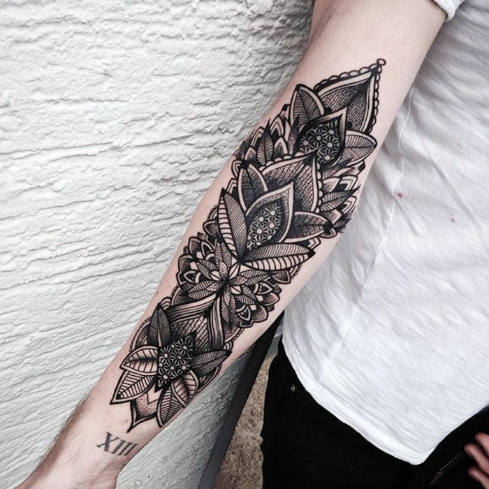 Mulher com tatuagem de antebraço no braço direito, tatuagem preta com motivos complexos, motivos de flores e folhas com muitas linhas, tatuagem com data, calças pretas com t-shirt branca