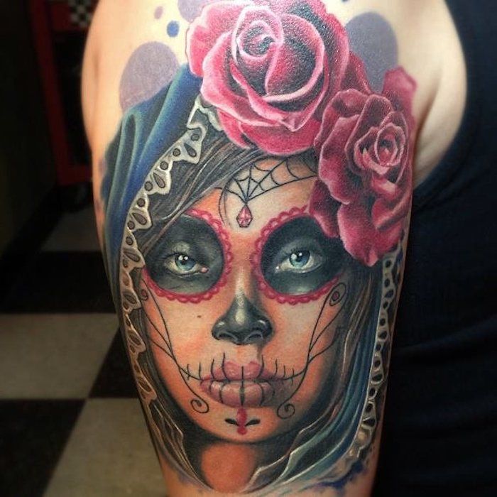 Hand met een tatoeage van een jonge overleden vrouw met rode lippen en een zwarte neus en een zwart spinnenweb en twee grote rode rozen
