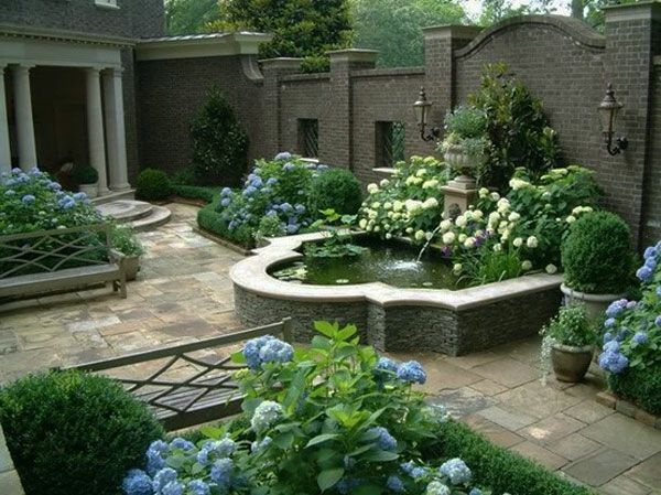 elegantiškas lauko baseinas, spalvingos gėlės ir akmens skulptūros sode