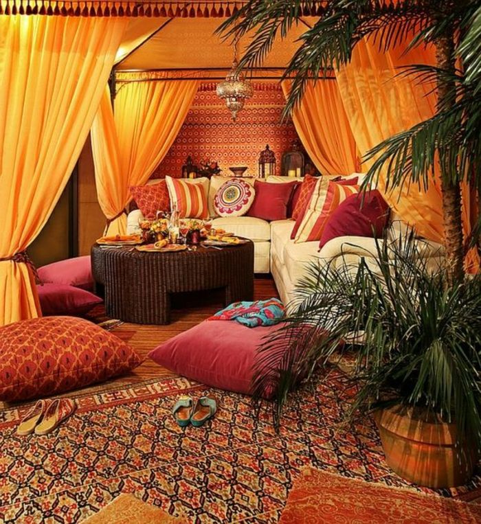 Sittegruppe med Baldahine med oransje gardiner, hvite sofaen er laget av lær, røde sofaen puter i untershiedlichen størrelser, runde Flechttisch i mørk brun, stor mønster teppe med en blomsterpotte på en stor og en liten palme, dekorative elementer av metall