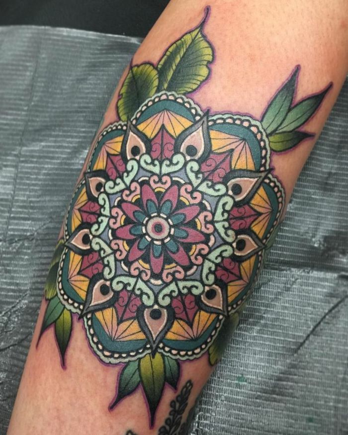 tatuagem colorida com muitos ornamentos e muitas folhas verdes, pontos brancos e contornos pretos