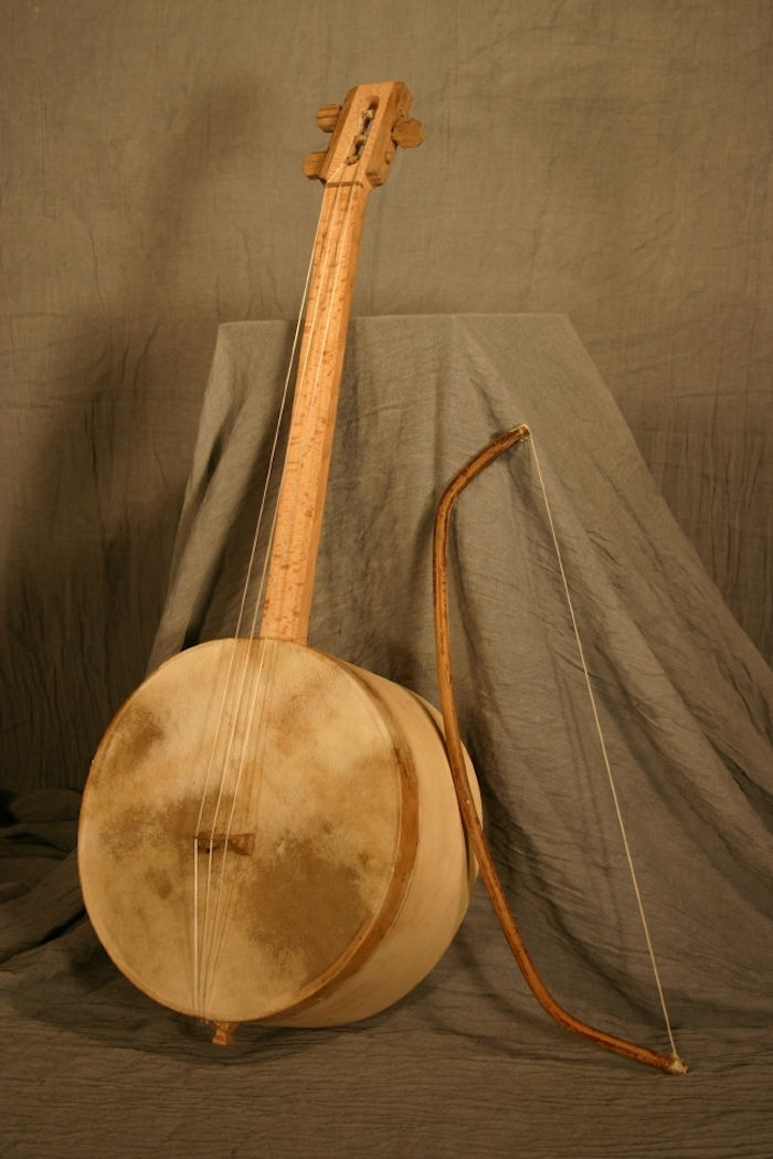 Chuniri din lemn de mesteacăn, cu corp rotund, pe care o bucată de piele cu pete întunecate este tensionată, un arc mare pentru instrumente îndoite