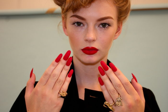 modello di donna unghie a punta gel con labbra rosse e unghie lunghe gel rosso anelli d'oro decorazione stile retrò acconciatura trucco