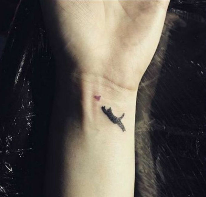 Aceasta este o mână cu un tatuaj mic, cu o pisică neagră și o pasăre - idee pentru un tatuaj pe o încheietura mâinii
