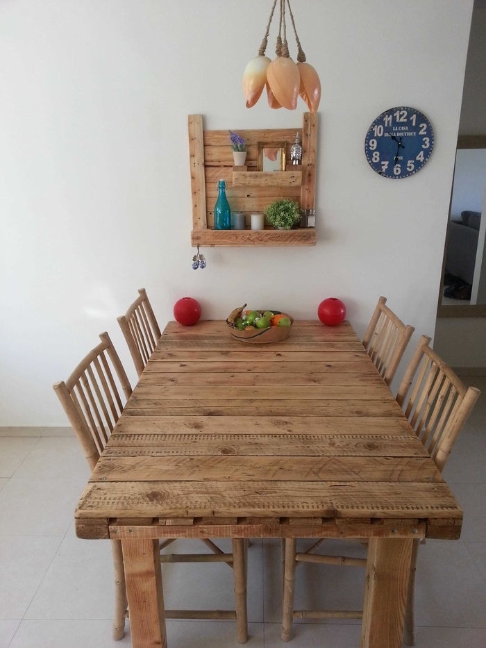 mesa de madeira, cadeiras de madeira e uma prateleira self-made de paletes e madeira com flores, uma foto e uma garrafa azul