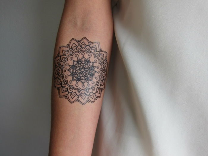 tatuaggio rotondo Mandala con molti ornamenti, tatuaggio color uovo sul lato interno del braccio di una donna, vestito con una camicetta di raso bianca
