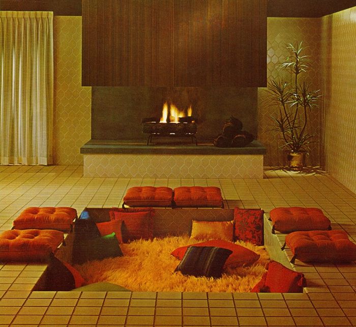 Japoński salon z prostym designem - nisko położony kącik relaksacyjny z pomarańczowymi poduszkami i żółtym dywanem, salon z kominkiem, otwarty palenisko z rośliną po prawej stronie