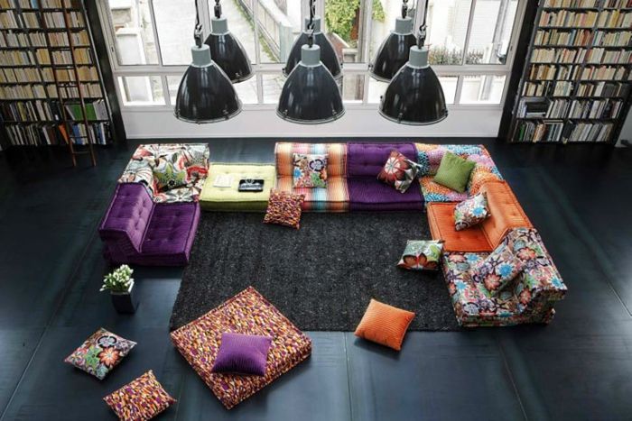 didžiulis gyvenamasis kambarys su dviem dideliais knygų Regalend iki lubų knygų lentynų su kopėčiomis, didelis minkštų sofos su medžiagomis, kurių skirtingų spalvų modelių, daug didelių ir mažų spalvotų sėdynė ir sofos pagalvėlių, juoda aukšte su juodu kilimu, šeši šviestuvai Pramoniniai Stilius
