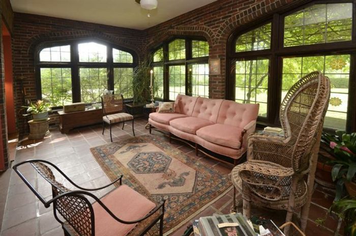 Cameră cu mobilier oriental în culori naturale, canapea roz cenușie cu cotiere, covor model în tonuri de pământ, casa cu pereți din cărămidă, ferestre mari