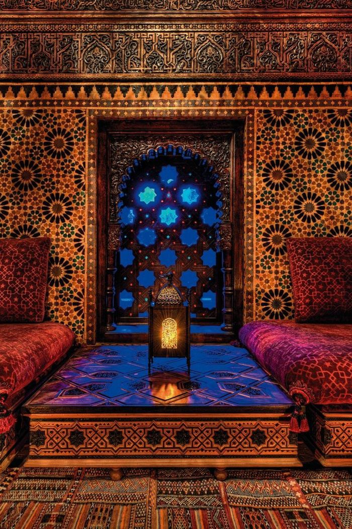 Camera cu un tapet de tapet oriental cu motive circulare, panouri de perete cu sculptură, două fotolii cu perne confortabile, cu ciucuri, masă cu desene, fereastră mică în formă de arc