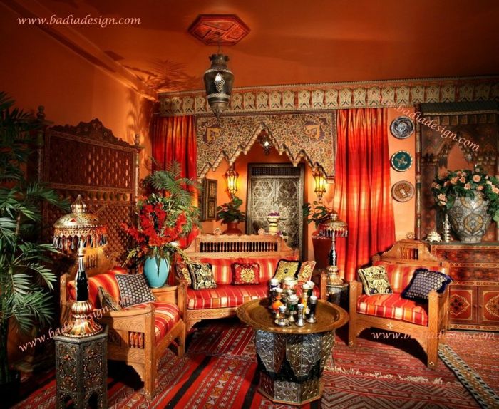 rikt dekorert i marokkansk stil, en sofa og to stoler laget av tre, puter med striper mønster, en kaffe og et bord med mange dekorasjoner, designer gulvlampe med metall skjerm, forgylte brett i rznder form, mange blomster og planter, to gardiner i rødt, vegger og tak malt i oransje, sammenleggbar skjerm laget av tre, tepper med ulike mønstre, kommode med en stor vase på tre dekorative veggplater