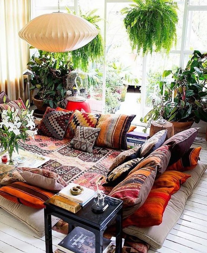 biała drewniana podłoga z małymi wzorami, marokańskie poduszki z kolorowymi wzorami, wiele zielonych roślin, dwie wiszące rośliny, białe papierowe żyrandole, kącik relaksacyjny z widokiem na taras