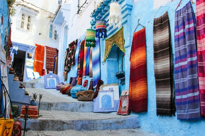 Niebieskie miasto w Maroku, ulica ze schodami - marokański rynek dekoracji i tkanin, chust i poszewek na poduszki, małe drewniane ozdobne pudełka i orientalne freski