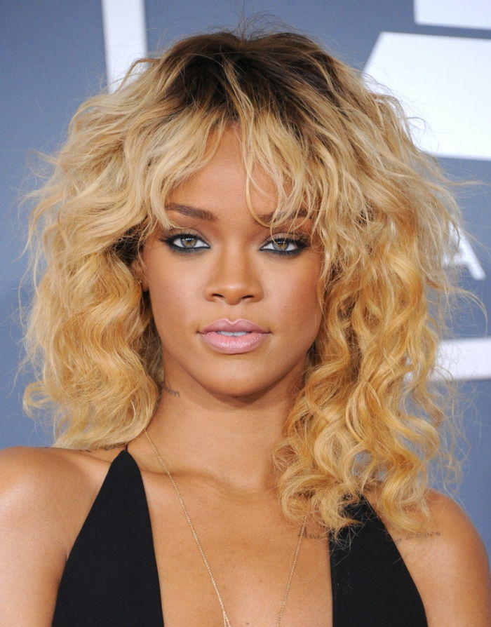 Rihanna med ponny frisyr, mörka blonda krullar, tråkiga läppar och svart mascara, svart aftonklänning