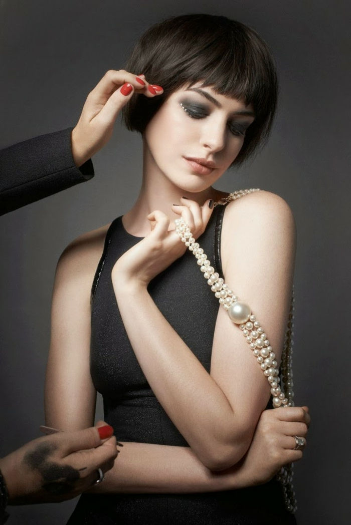 Anne Hathaway z krótką fryzurą kucyka, tępymi wargami i smokey eyes, czarną sukienką, perłami