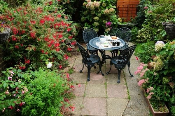 gražus sodas su daugybe spalvingų gėlių ir nedidelis žurnalinis stalas su keturiais kėdėmis