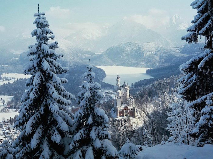 romantická zimná scéna s bielym zámkom s vežami a lesom s množstvom stromov - hory so snehom - modrú oblohu s bielymi oblaky