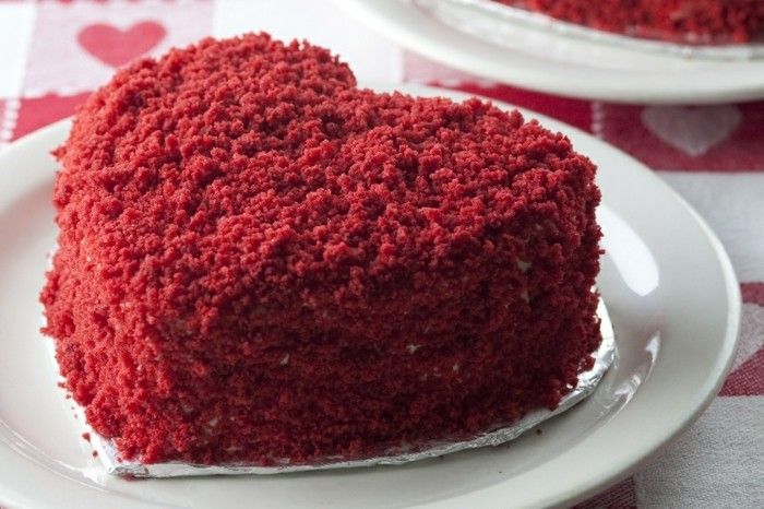 röd-sammet kaka-i-formen-av-en-heart-shape-med-röd-smulor-dekorerade-hjärta kaka-valentin