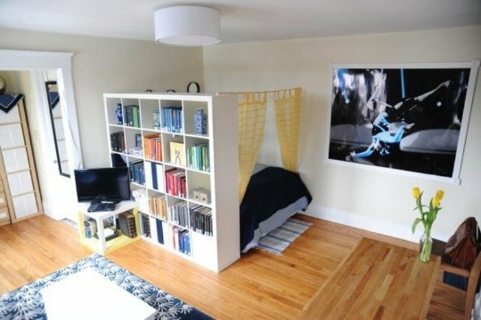 sovrum, vardagsrum-rumsavdelare-shelf-hyllan-utrymme Trenner-böcker hylla-rumsavdelare-trägolv mönster matta sovrum-dubbelsäng Tv