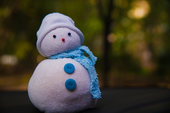 malý biely snehuliak s dvoma modrými gombíkmi, dvoma čiernymi očami a bielym klobúkom - robia z ponožiek snehuliaka