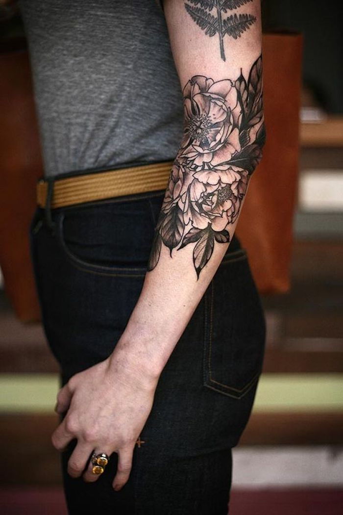 piękne tatuaże, kobieta z czarnymi dżinsami, szara bluzka i tatuaż z kwiatami