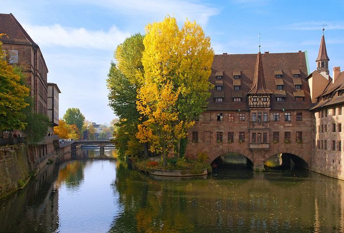 de vackraste semesterdestinationerna i Bayern, Tyskland floden och byggnader i floden eller över bron höst träd i gul orange och grön