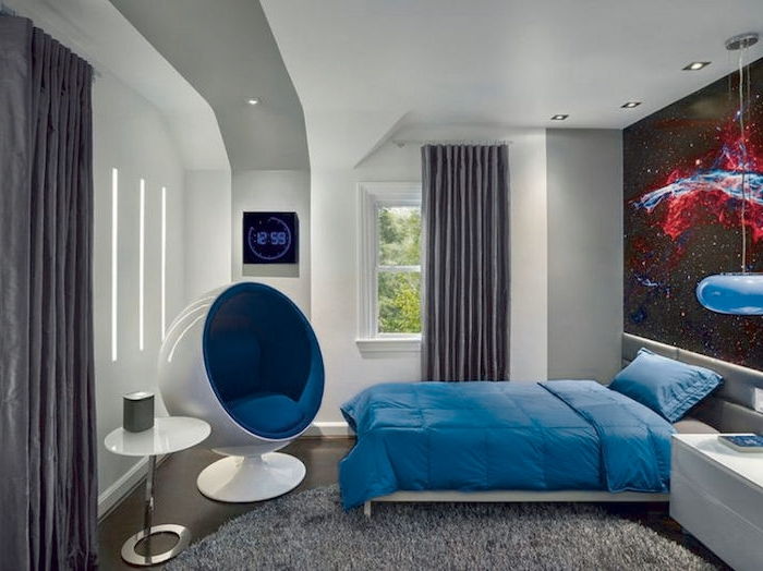 apvalus pilkas kilimas, mėlynas linas, baltas stalas ir modernus fotelis - jaunimo kambario dizainas