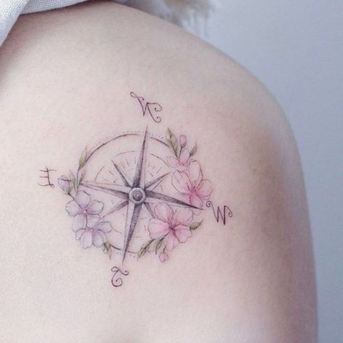 un tatuaj foarte frumos, cu flori roz și violete și o busolă pe spate