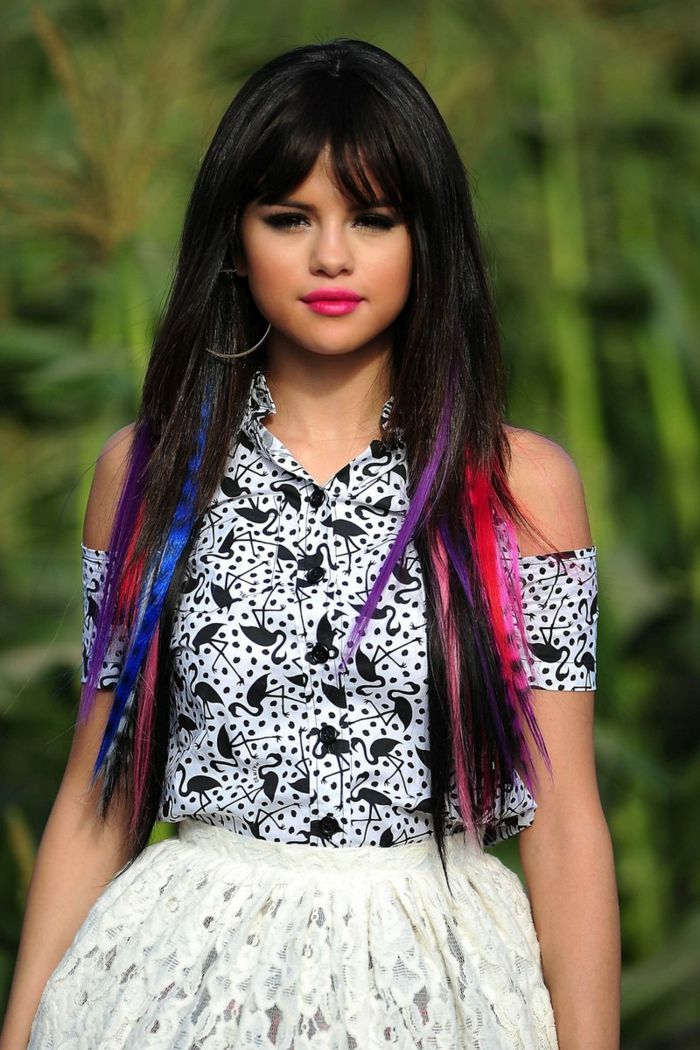 Selena Gomez com fios coloridos, cabelos longos com franja, batom claro, rímel preto