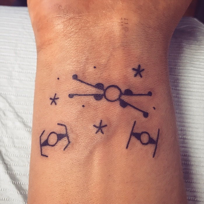 un tatuaj mic mic de nave spatiale zburatoare si mici stele si planete negre