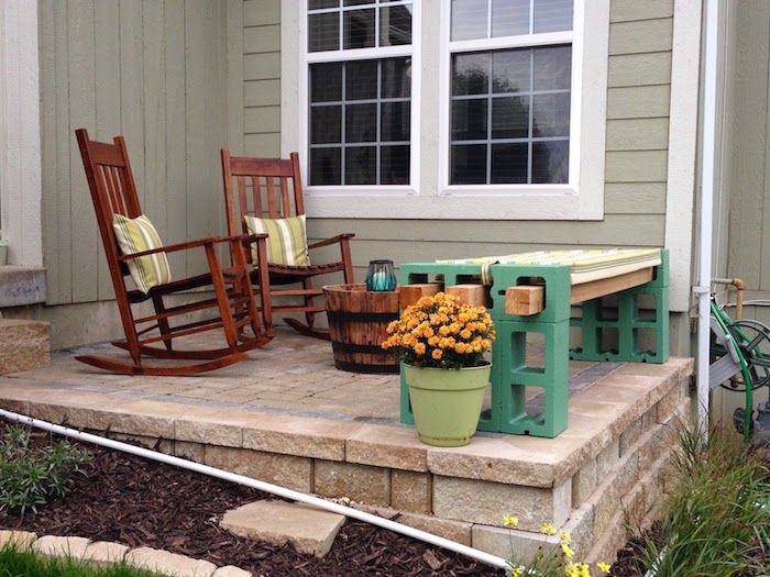 hus med terrass - två bruna stolar med gröna kuddar - blomkruka med apelsinblommor - en grön trädgårdsbänk av gröna växtstenar