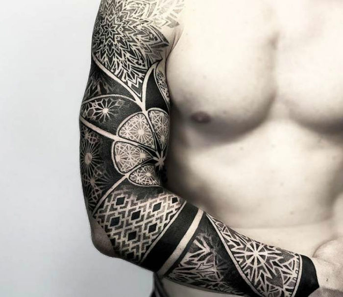 Uomo con tatuaggio a manica con un motivo floreale e molti motivi geometrici e spesse linee bianche e nere, l'uomo tatuato con tutto il suo braccio