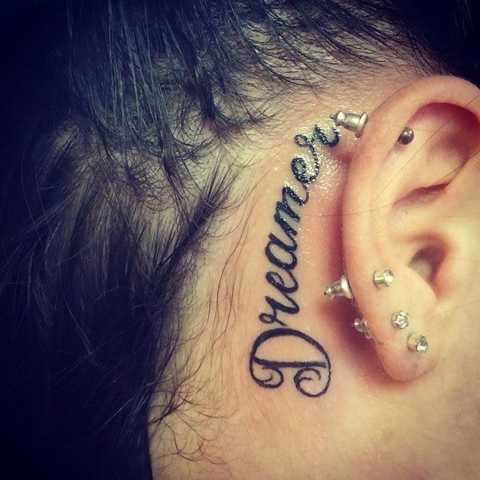 Drobni črni tatoo sanjar za ušesom mlade ženske