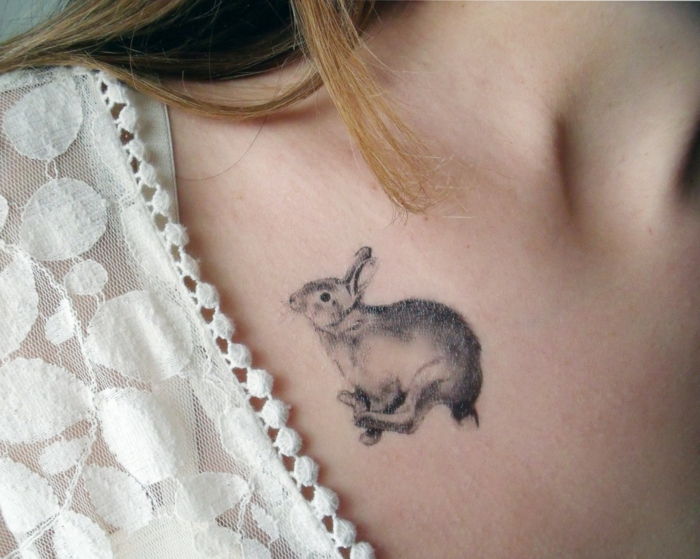 Motivo di tatuaggi piccolo coniglietto che salta sulla spalla di una decorazione di camicetta di pizzo capelli donna bionda