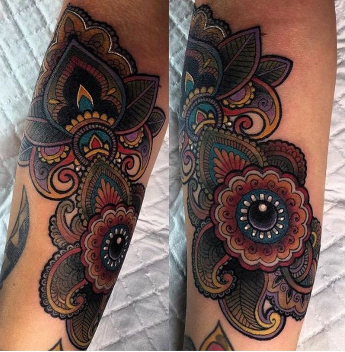 donkere tatoeage met veel spiralen, witte druppel- en oogmotieven, mandala in donkere kleuren met gele, rode en blauwe ornamenten