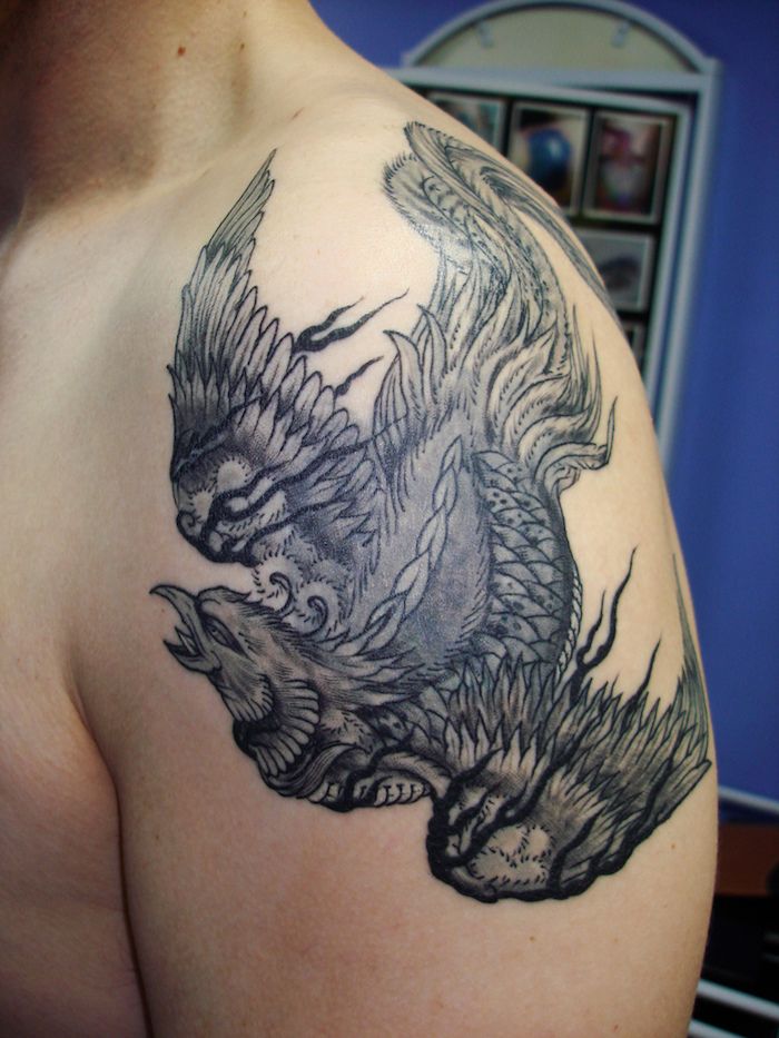 vyras su ranka, turinčia juodą tatuiruotę su plaukiojančiu juodu feniiksu su baltomis ir juodosiomis plunksnomis - vyrų tatuiruotė su phoenix
