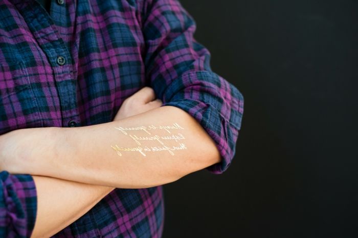tatuaje frumoase cuvinte de aur stând pe braț și înfrumusețează cămașa violet albastru
