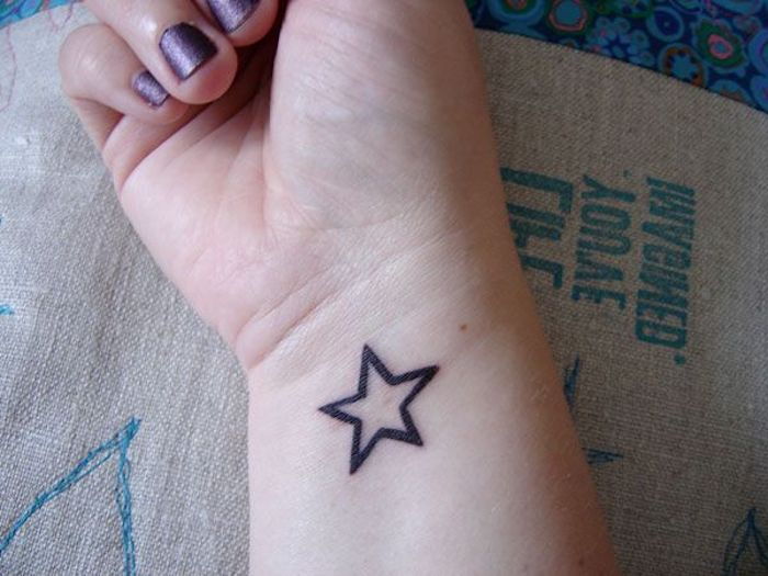 Ruku s purpurovým lakom na nechty a malým čiernym hviezdnym tetovaním