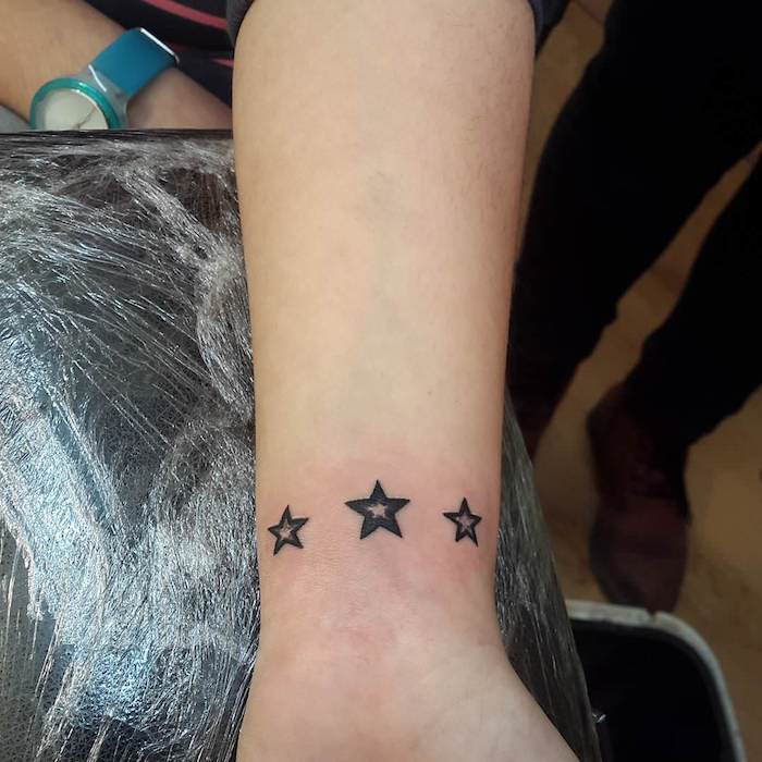 En hånd som holder en svart tatoveringsstjerne med tre små svarte stjerne tattoo stjerne håndledd