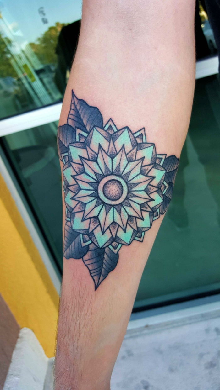 Tatuaż w kształcie trójkąta z granatowymi liśćmi i turkusowym środkiem. Kobieta z tatuażem kolorowe ramię