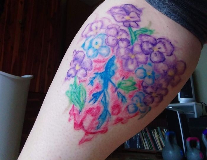 lila och blå blommor på röd bakgrund på ben akvarell tatuering
