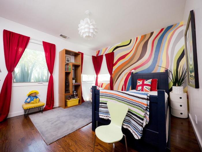 raudonos užuolaidos, spalvinga siena, maža lova su raštuotas pagalvėmis - gražus kambarys
