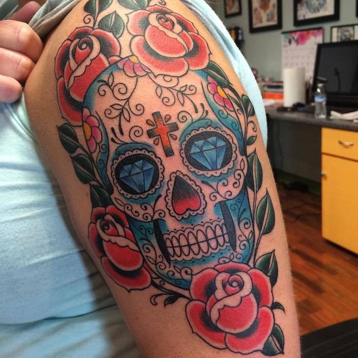 Meksikos kaukolės tatuiruotė su mėlynais deimantais ir baltais dantukais bei oranžinės kryžiaus ir violetinės gėlės - kaukolė su rožių tatuiruotėmis